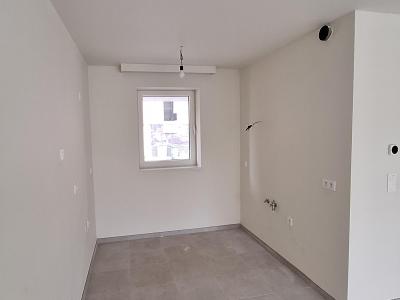 Open keukenruimte met witte muren, grijze tegelvloer en één raam dat zorgt voor natuurlijk licht